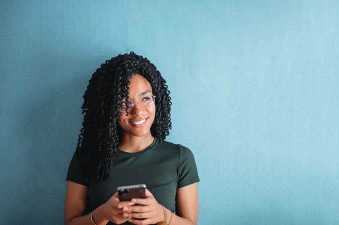 Black womxn with a professional, defined locs afro hairstyle wearing glasses and holding a mobile phone in her hands