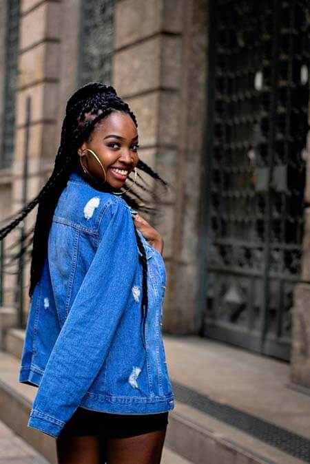 Black womxn with a professional jumbo braids hairstyle partly gathered in ponytail turning to the camera and smiling