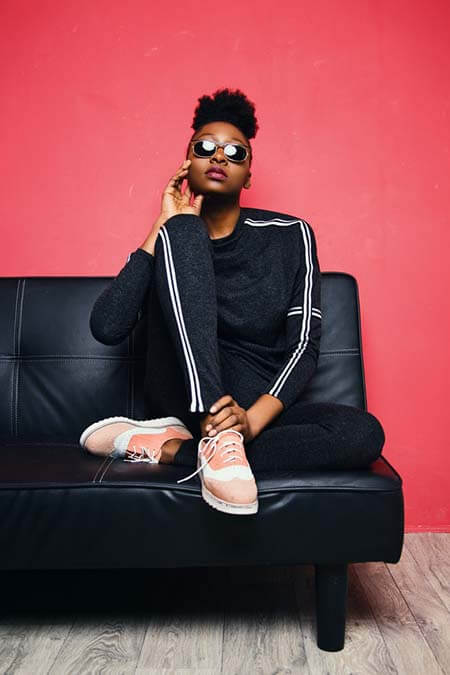 Black womxn with a professional afro textured puff hairstyle wearing sunglasses, sitting on a black leather couch