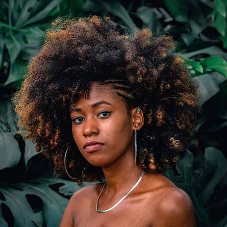 Black womxn with a professional big afro with highlights and half braided left side hairstyle wearing big silver hoops and necklace